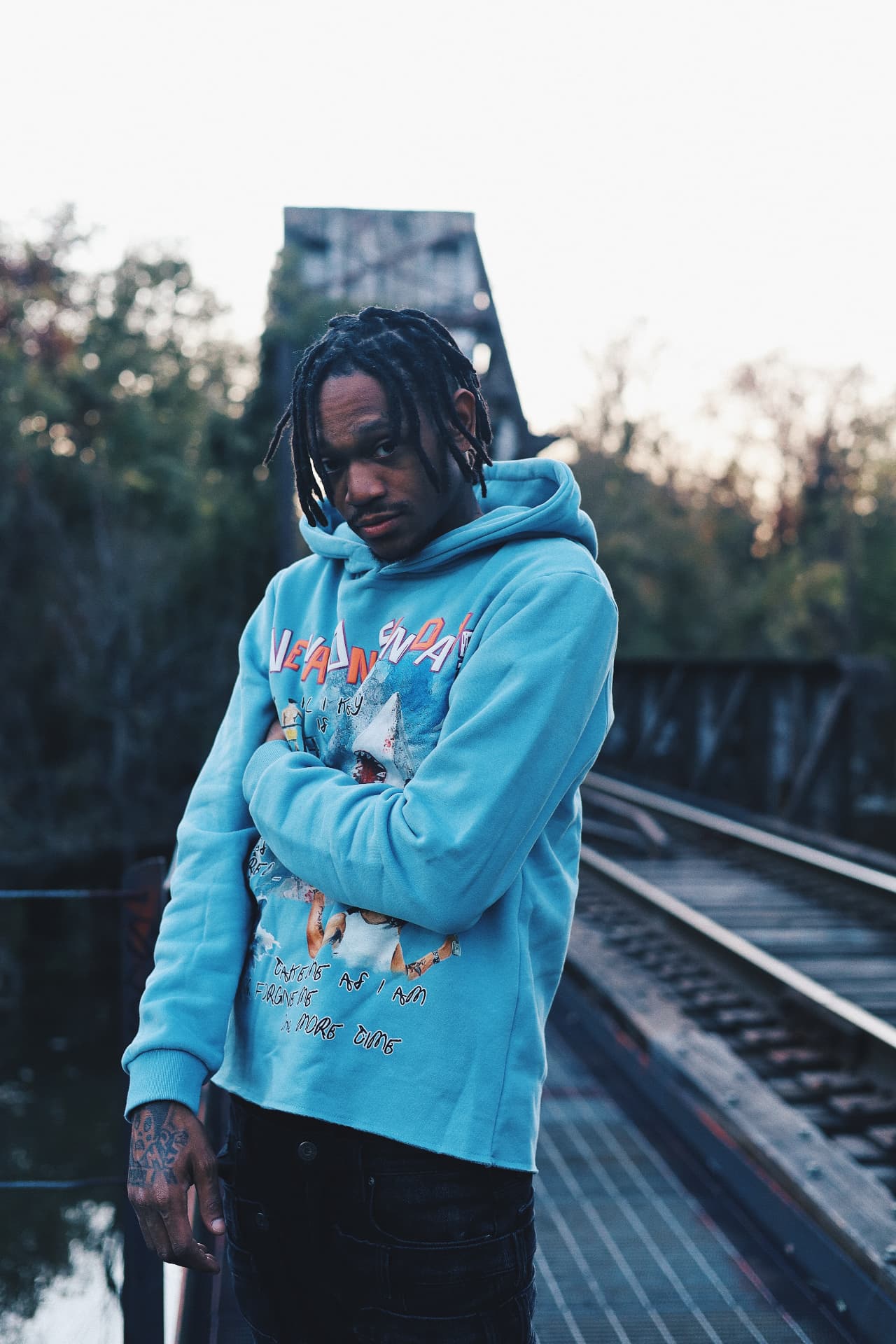 Luh Kiddo standing on railway tracks in a light blue hoodie